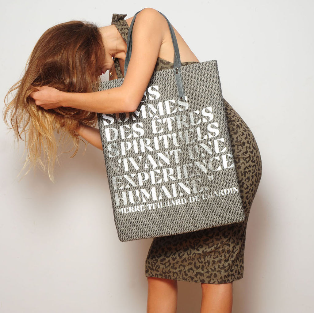 HIGH BAG #27 EVA ZINGONI | Tweed | Nous sommes argent graphique  https://www.evazingoni.fr/products/copie-de-high-bag-6-soie-fleurs-vertes-nous-sommes-or-graphique  Sac cabas luxe en tweed de laine gris et cuir gris. Citation philosophique en coloris argent "Nous sommes des êtres spirituels vivant une expérience humaine." de Pierre Teilhard de Chardin. Eco-friendly tote bag. Tweed tote bag